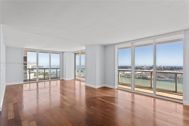 spare room with hardwood / wood-style floors, a wall of windows, and a water view