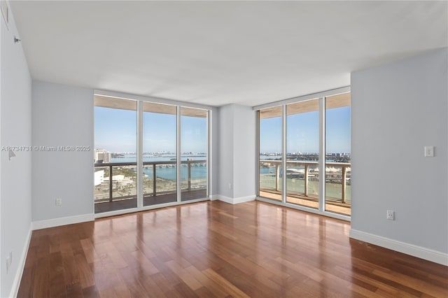 unfurnished room with expansive windows, wood-type flooring, a water view, and a wealth of natural light