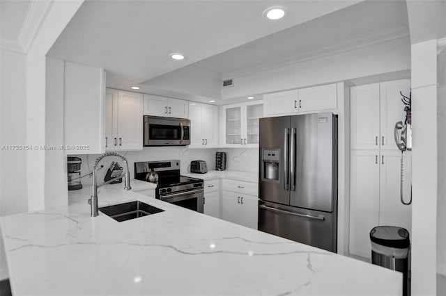 kitchen featuring appliances with stainless steel finishes, white cabinetry, sink, kitchen peninsula, and light stone countertops