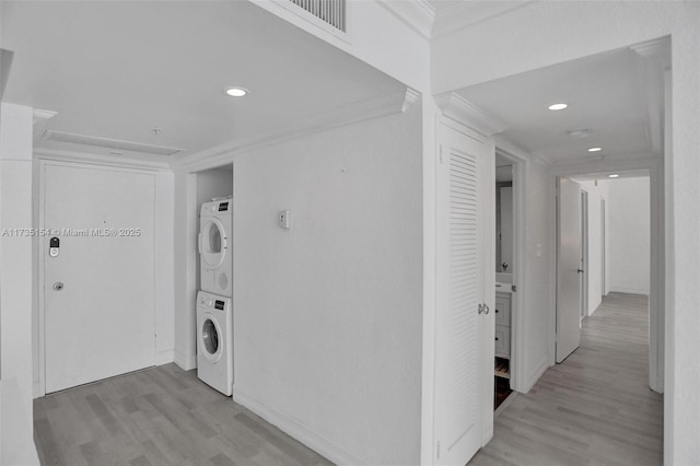 washroom with crown molding, stacked washer and clothes dryer, and light wood-type flooring