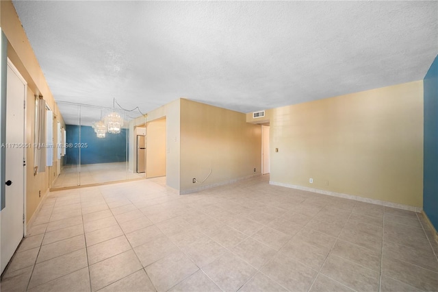 unfurnished room featuring an inviting chandelier, a textured ceiling, and light tile patterned floors