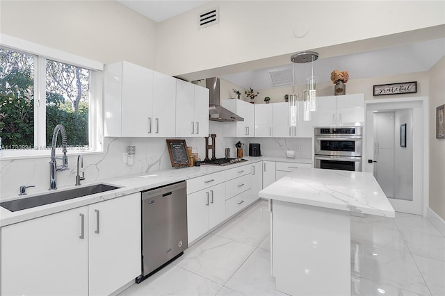 kitchen featuring white cabinetry, appliances with stainless steel finishes, wall chimney exhaust hood, and hanging light fixtures