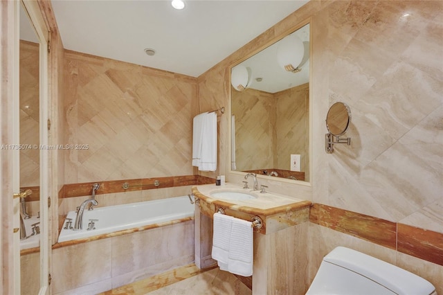 bathroom with tile walls, vanity, tiled bath, and toilet