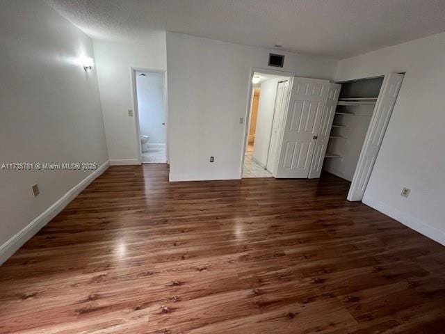 unfurnished bedroom with dark wood-type flooring, a closet, connected bathroom, and a textured ceiling