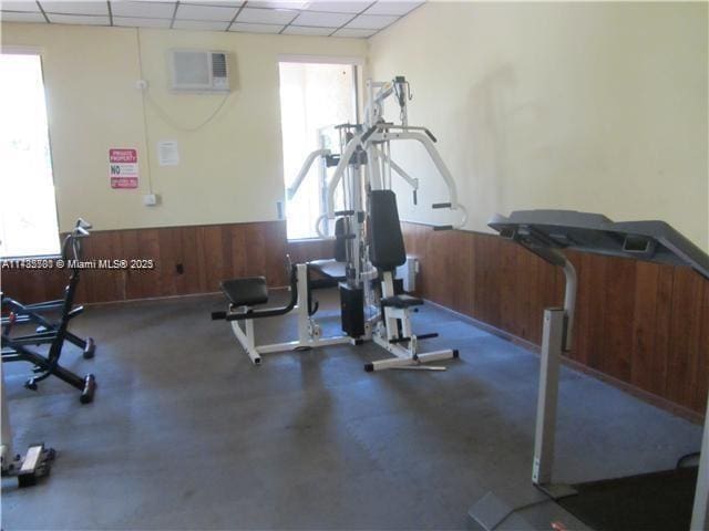 exercise room featuring a wall mounted air conditioner, wooden walls, and a drop ceiling