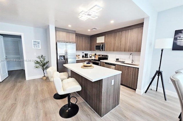 kitchen with modern cabinets, a sink, a kitchen island, appliances with stainless steel finishes, and a breakfast bar area