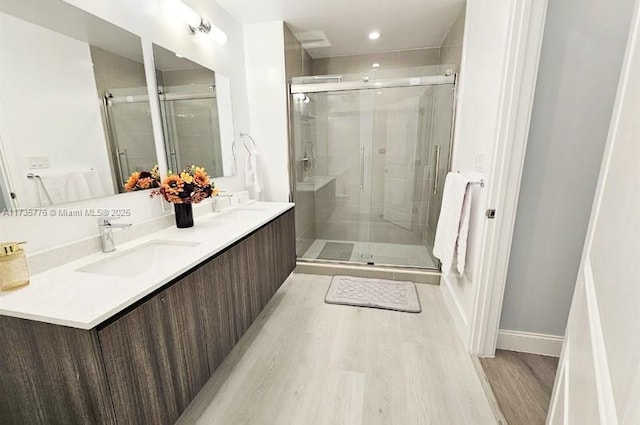 bathroom with a sink, a stall shower, wood finished floors, and double vanity