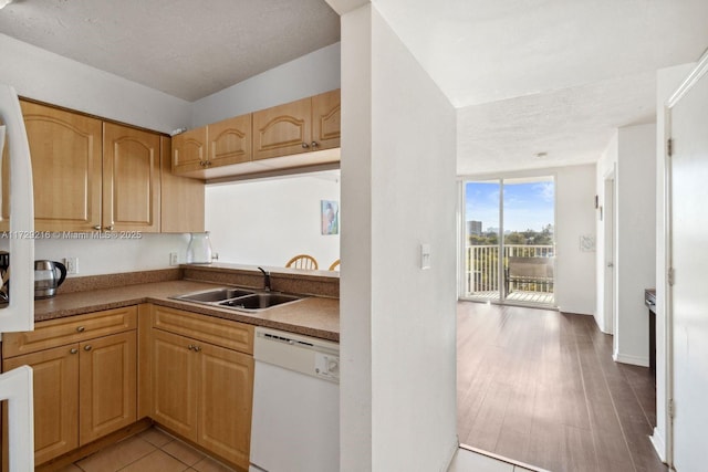 kitchen with dishwasher, sink, light wood-type flooring, light brown cabinets, and a textured ceiling