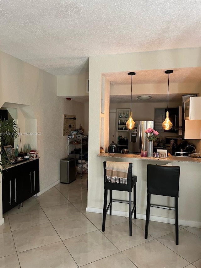 kitchen with a breakfast bar, pendant lighting, kitchen peninsula, stainless steel refrigerator with ice dispenser, and a textured ceiling