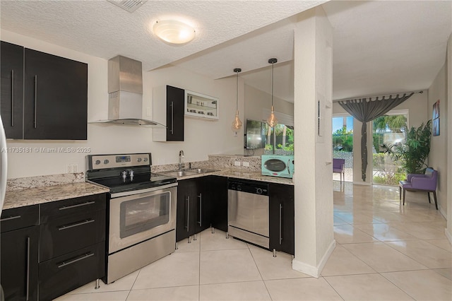 kitchen with stainless steel appliances, light tile patterned flooring, a sink, wall chimney range hood, and dark cabinetry