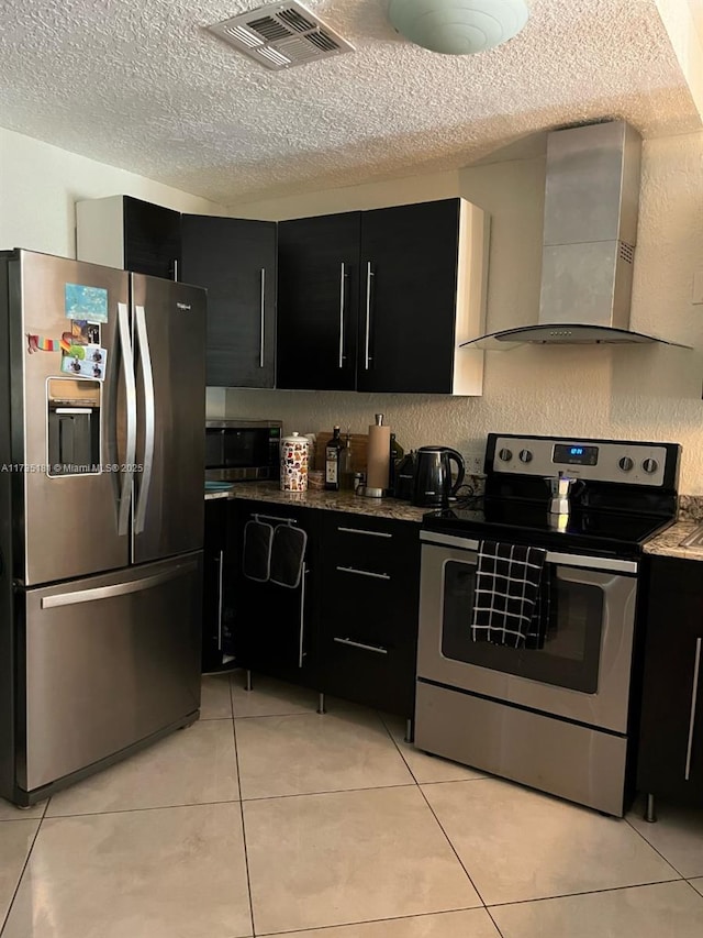 kitchen with light tile patterned flooring, appliances with stainless steel finishes, wall chimney range hood, and a textured ceiling