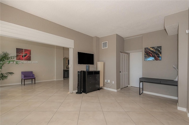 living area with light tile patterned floors, a textured ceiling, visible vents, and baseboards