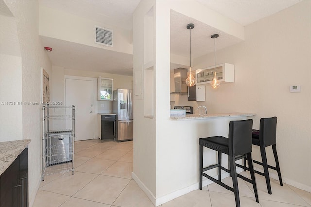 kitchen featuring stainless steel fridge, visible vents, a kitchen breakfast bar, and light tile patterned flooring