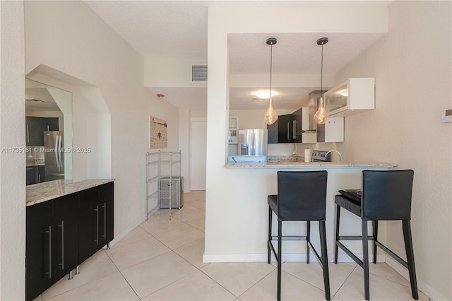 kitchen featuring stainless steel refrigerator with ice dispenser, visible vents, freestanding refrigerator, dark cabinetry, and a kitchen breakfast bar