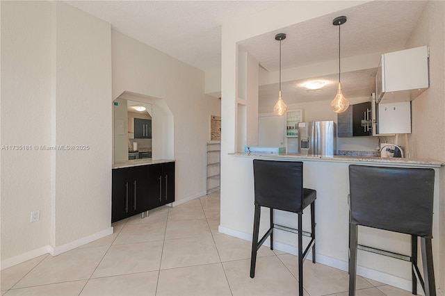 kitchen featuring light tile patterned flooring, light countertops, hanging light fixtures, stainless steel refrigerator with ice dispenser, and a kitchen bar