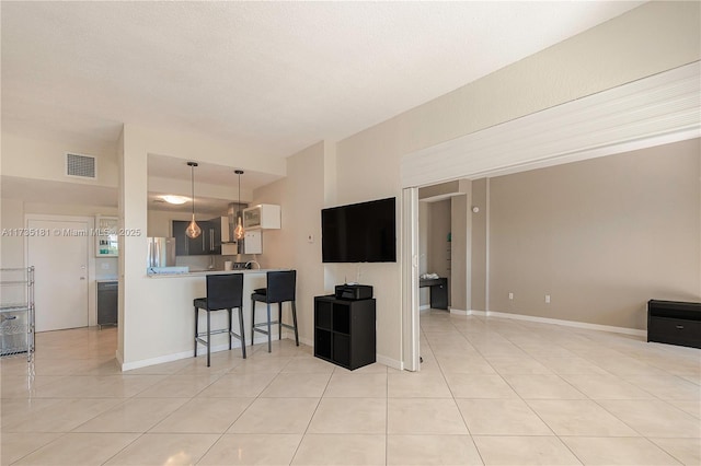 interior space featuring light tile patterned flooring, visible vents, a kitchen breakfast bar, and freestanding refrigerator