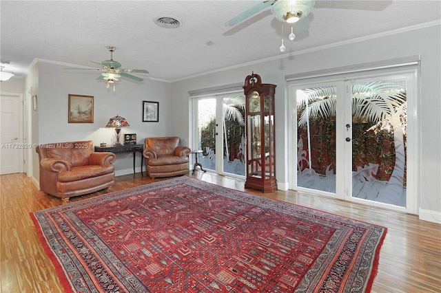 living area with a textured ceiling, wood finished floors, visible vents, french doors, and ornamental molding