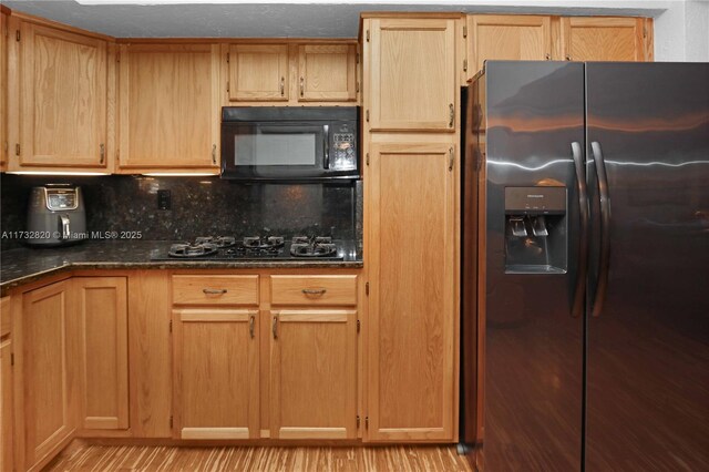 kitchen featuring decorative backsplash, light hardwood / wood-style flooring, black appliances, and dark stone counters