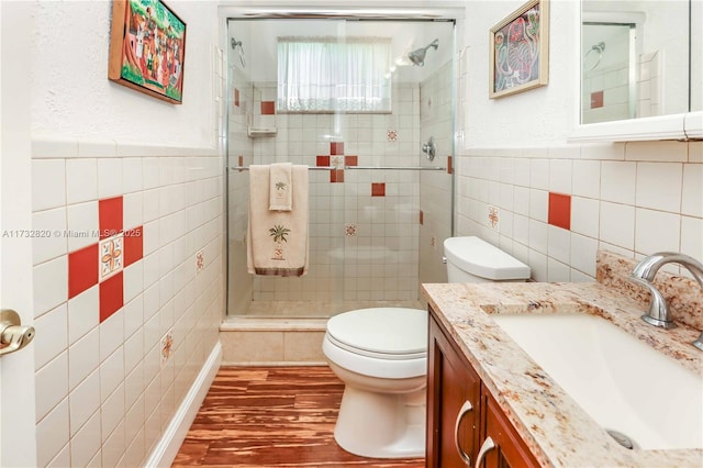 full bathroom featuring a wainscoted wall, tile walls, toilet, a shower stall, and wood finished floors