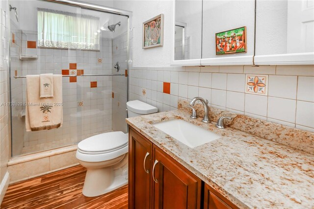 bathroom featuring toilet, an enclosed shower, wood-type flooring, tile walls, and vanity