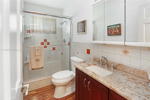 bathroom with tile walls, toilet, vanity, a shower stall, and wood finished floors