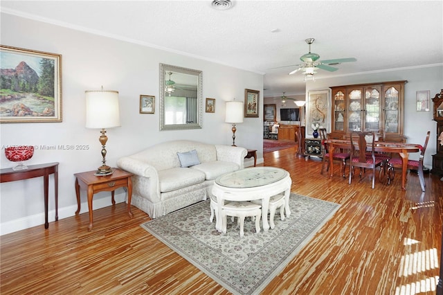 living room featuring crown molding, ceiling fan, a textured ceiling, wood finished floors, and baseboards