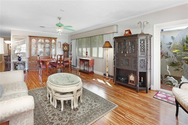 living area featuring baseboards, a ceiling fan, ornamental molding, wood finished floors, and a textured ceiling