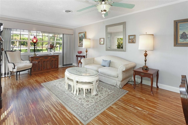 living room with a textured ceiling, wood finished floors, visible vents, baseboards, and ornamental molding