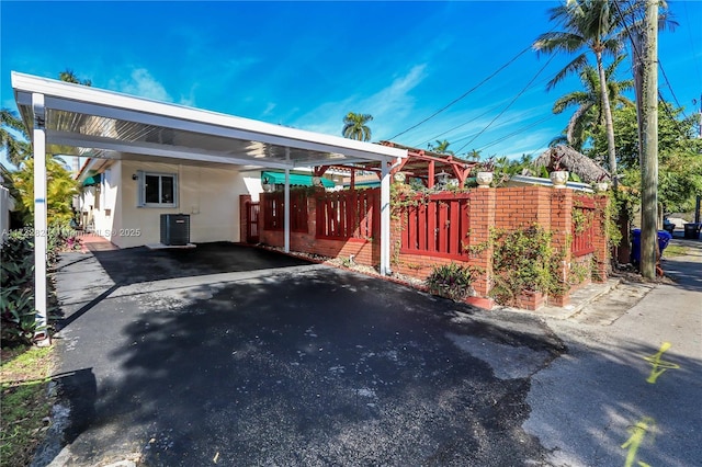 exterior space featuring a carport, stucco siding, fence, and central AC unit