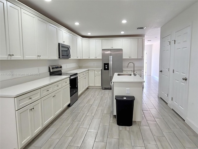 kitchen featuring a kitchen island with sink, stainless steel appliances, a sink, white cabinetry, and light countertops