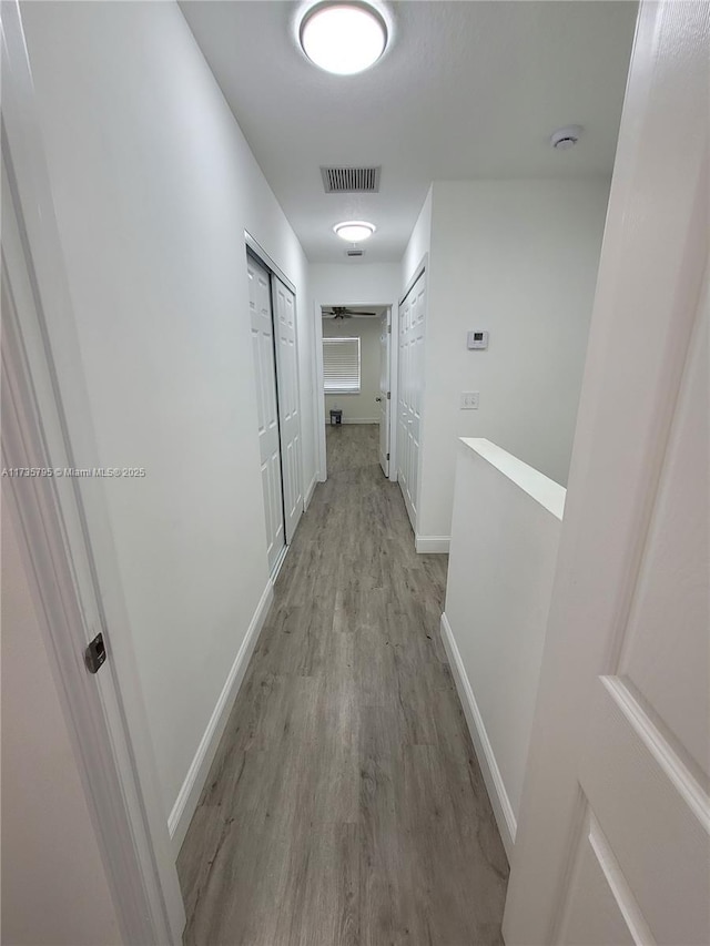 hall with an upstairs landing, visible vents, light wood-style flooring, and baseboards