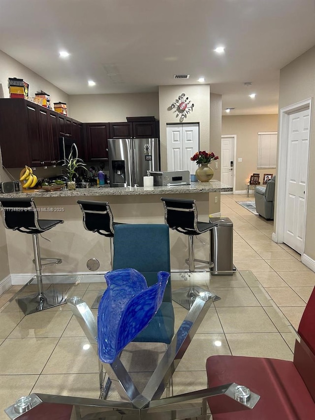 kitchen featuring a breakfast bar, stainless steel fridge with ice dispenser, light stone countertops, and light tile patterned floors