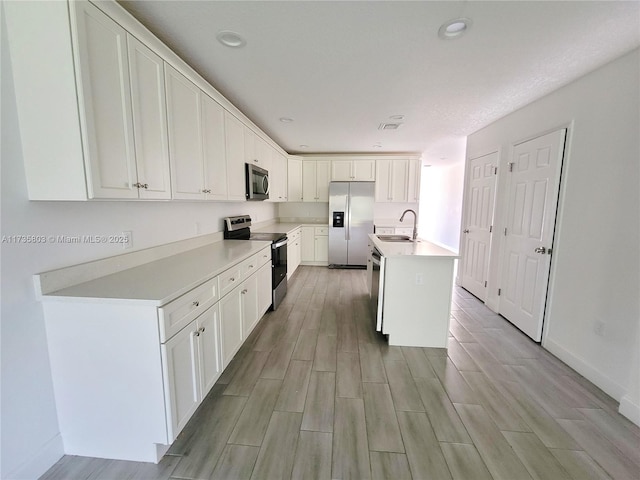 kitchen with a kitchen island with sink, stainless steel appliances, a sink, white cabinets, and light countertops