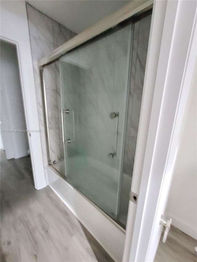 full bathroom with combined bath / shower with glass door and wood finished floors