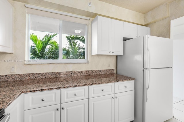 kitchen with white refrigerator, dark stone countertops, and white cabinets