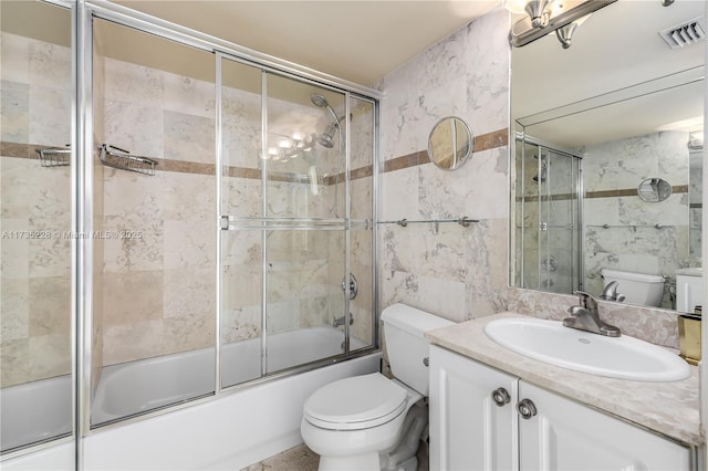 full bathroom featuring bath / shower combo with glass door, tile walls, vanity, and toilet