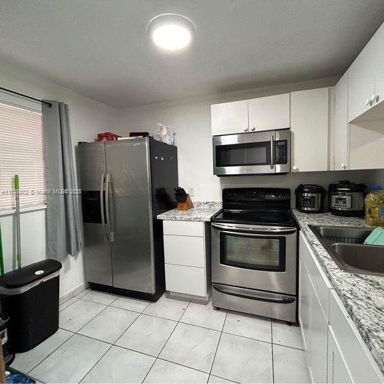 kitchen with appliances with stainless steel finishes, light stone countertops, sink, and white cabinets