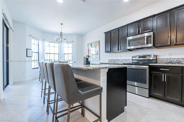 kitchen featuring pendant lighting, a kitchen bar, a center island, light stone counters, and stainless steel appliances