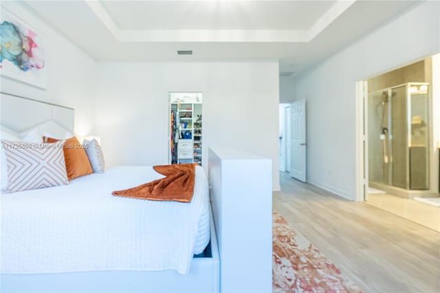 bedroom with a walk in closet, connected bathroom, a raised ceiling, and light hardwood / wood-style floors