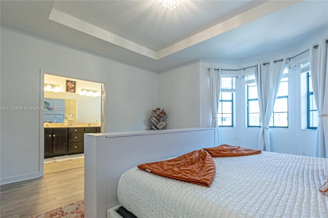 bedroom with connected bathroom, a raised ceiling, and light hardwood / wood-style floors