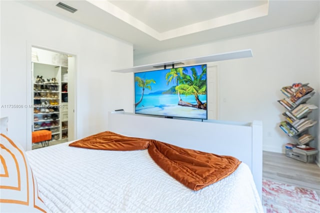 bedroom with a raised ceiling, wood-type flooring, and a closet