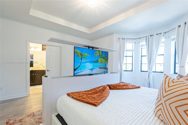 bedroom featuring a tray ceiling, light hardwood / wood-style flooring, and ensuite bathroom