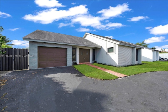 view of front facade featuring brick siding, fence, a garage, driveway, and a front lawn