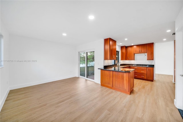 kitchen featuring light wood-style flooring, a peninsula, open floor plan, brown cabinetry, and dark countertops