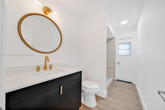 bathroom featuring hardwood / wood-style flooring, vanity, tiled shower, and toilet