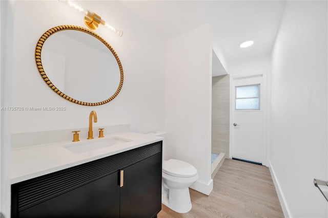 bathroom with toilet, a tile shower, vanity, wood finished floors, and baseboards