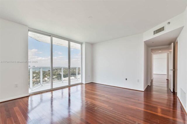 empty room with a wall of windows and dark hardwood / wood-style floors