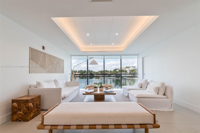 living room featuring a tray ceiling, floor to ceiling windows, and a water view