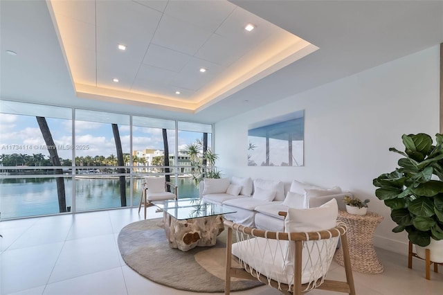 common area featuring a wall of windows, a water view, a tray ceiling, and light tile patterned flooring