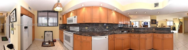 kitchen featuring light tile patterned floors, sink, white appliances, kitchen peninsula, and dark stone counters